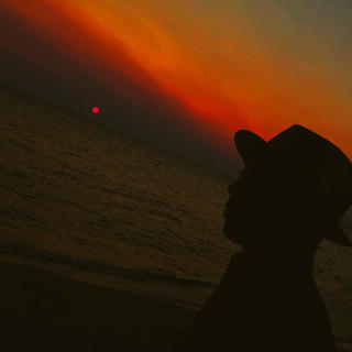 Silhouette of person in hat against dramatic orange and amber sunset over water
